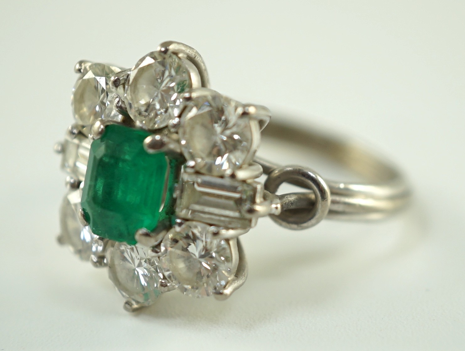 A mid 20th century 18kt white gold, single stone emerald and round and baguette cut diamond cluster ring